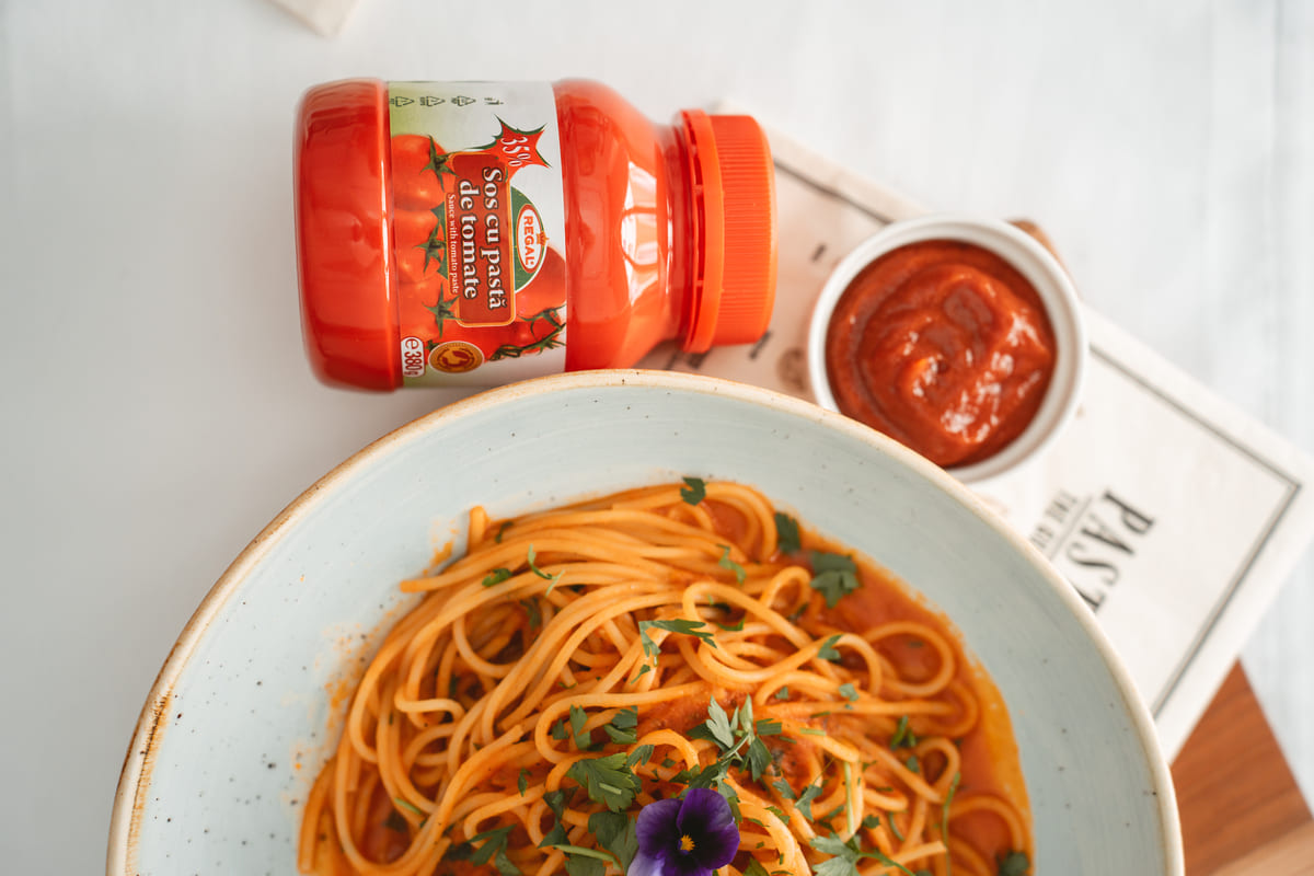 Sos cu pasta de tomate regal langa o farfurie de spaghetti