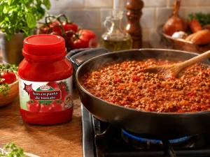 Sos bolognese cu carne tocată gătit într-o tigaie pe aragaz, alături de borcanul Regal sos cu pastă de tomate de 540 g.