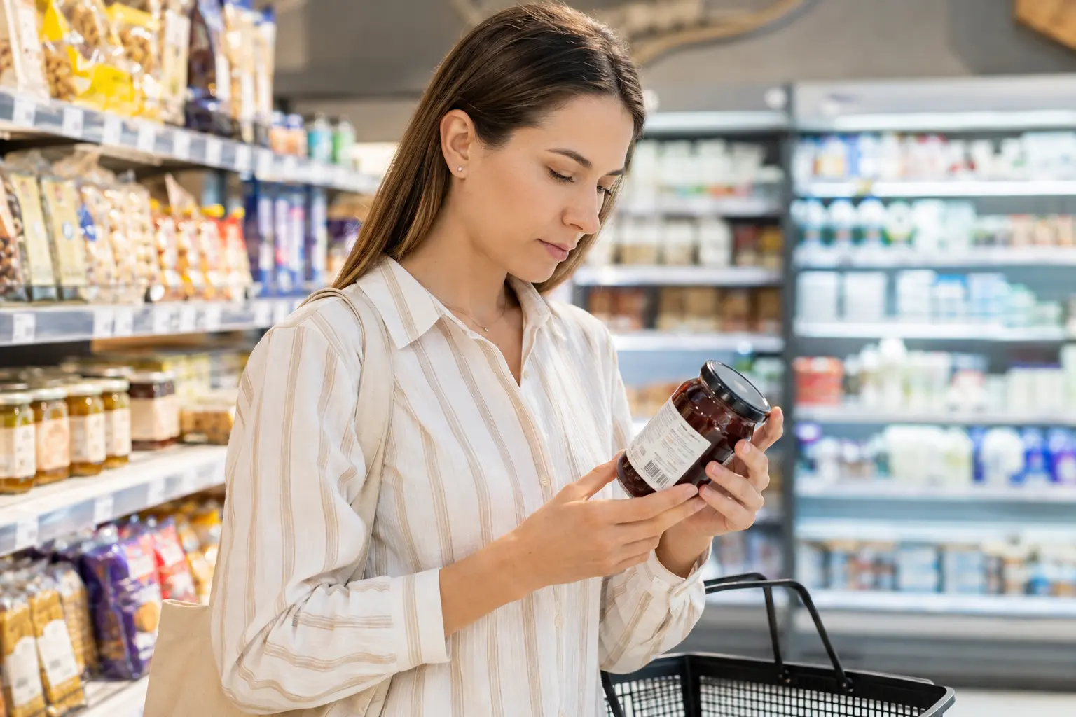 Femeie într-un supermarket care citește eticheta unui produs dulce, ilustrând verificarea informațiilor nutriționale înainte de cumpărare.