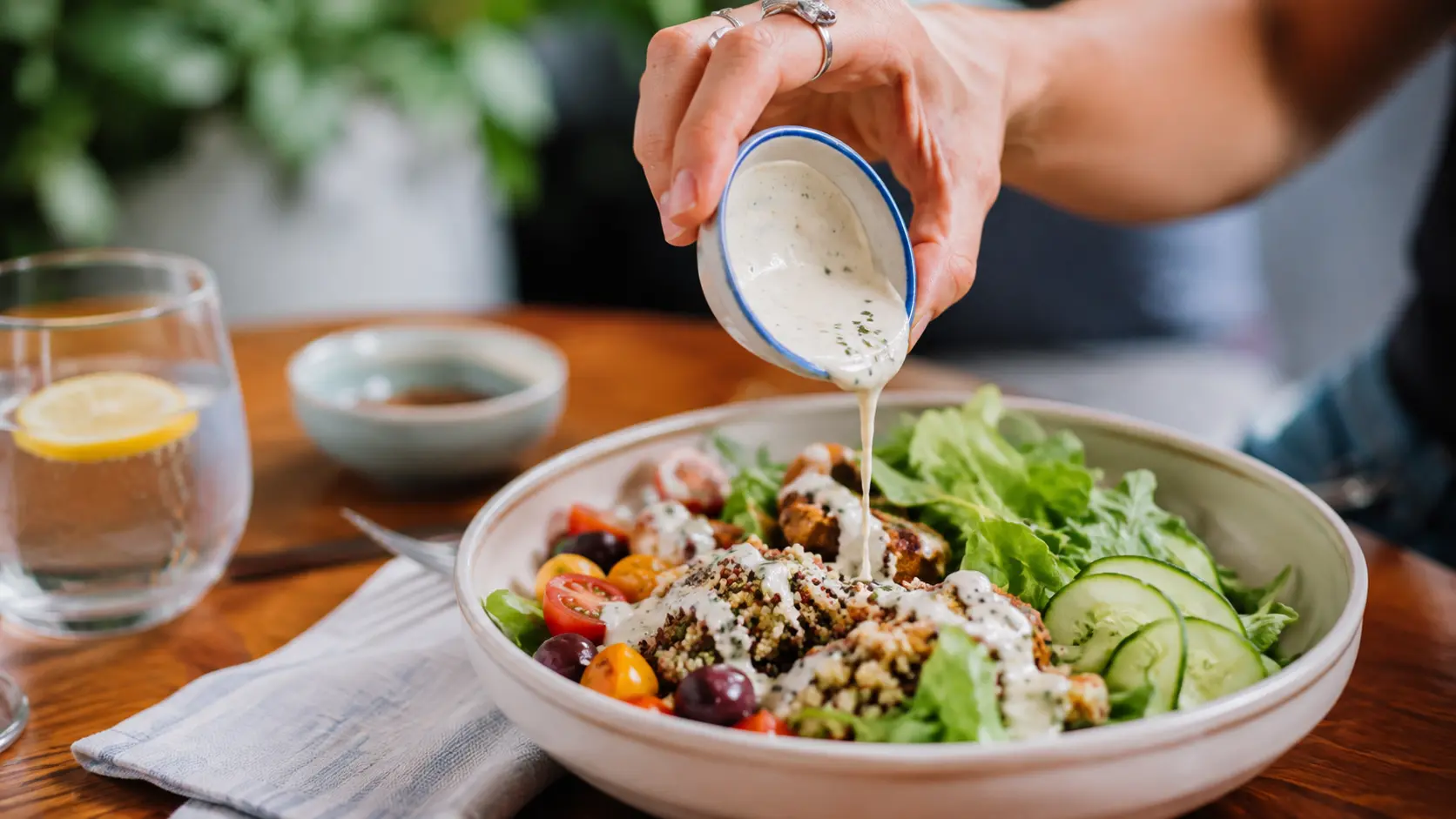 Dressing cremos turnat peste o salată proaspătă, cu legume și frunze verzi, într-un bol.
