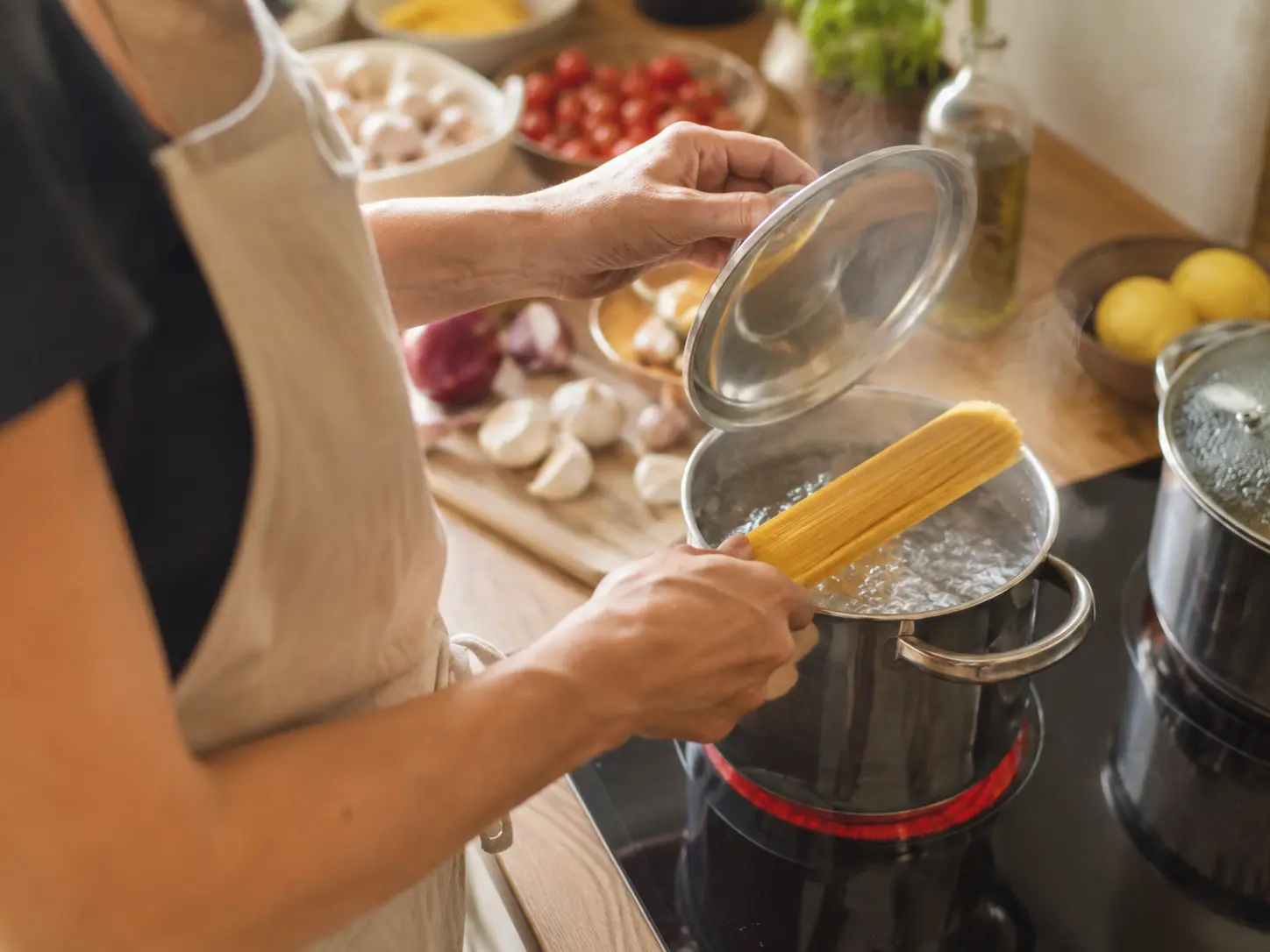 Persoană care gătește paste într-o oală, într-o bucătărie de acasă, ilustrând utilizarea produselor culinare pentru gătitul zilnic.